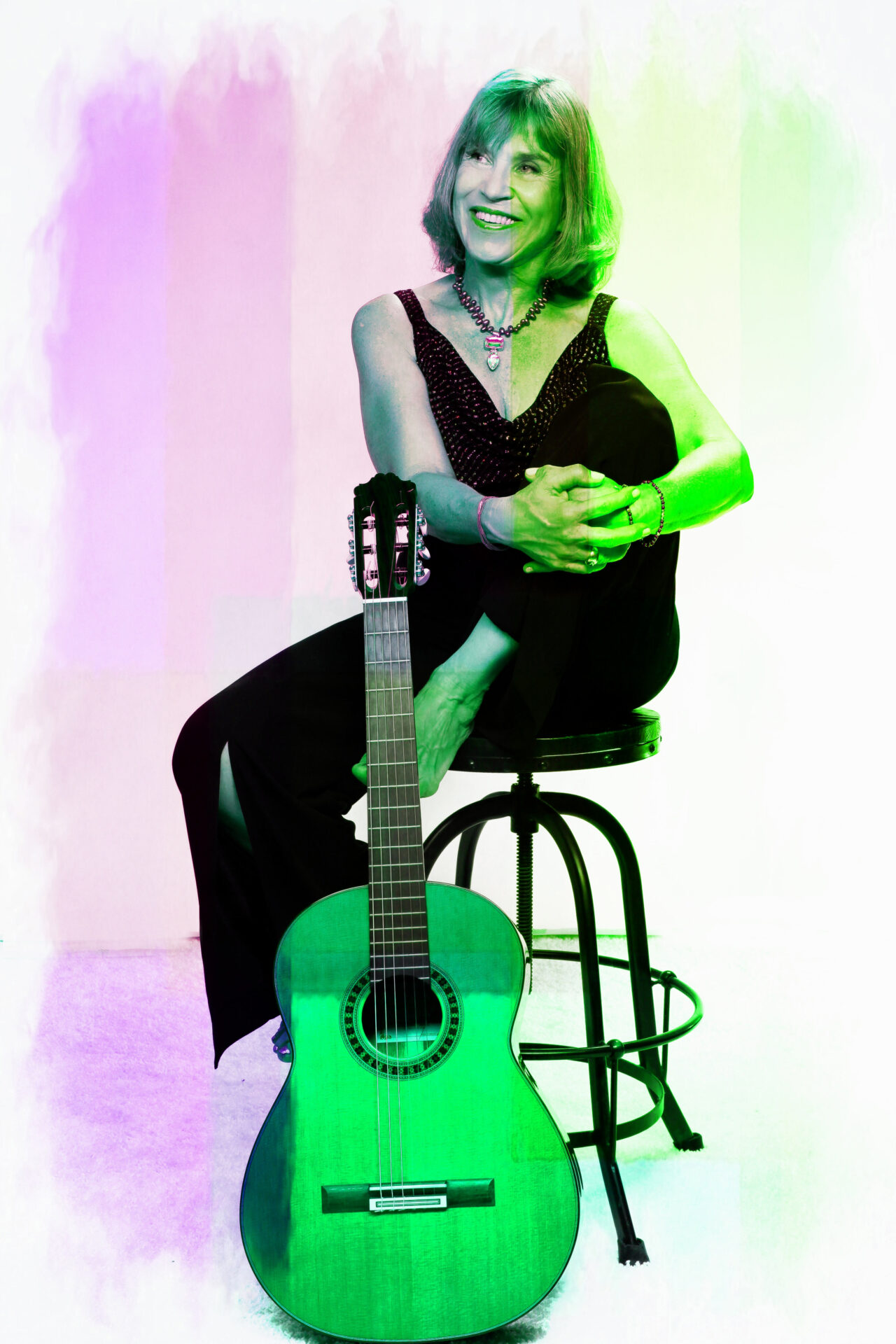 A woman sitting on a stool with a green acoustic guitar.