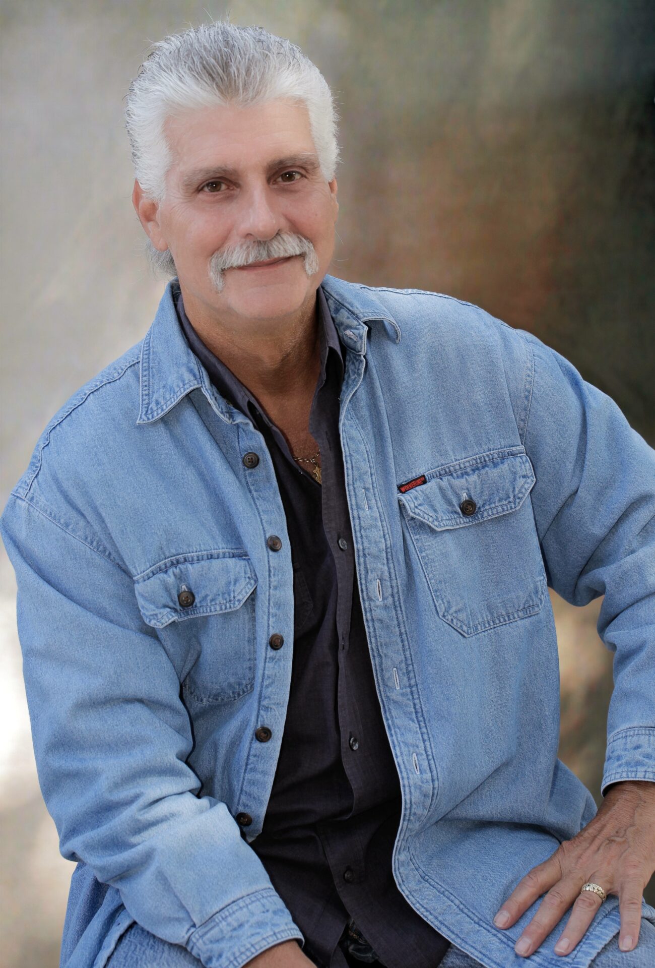 A man in a denim shirt is posing for a photo.